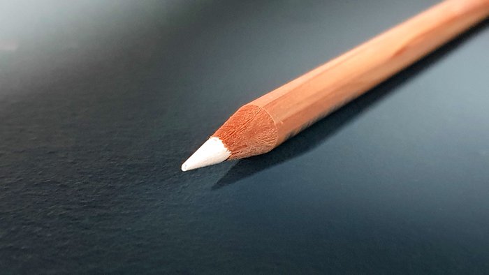 tip of a white caran d'ache colored pencil on dark blue grey background